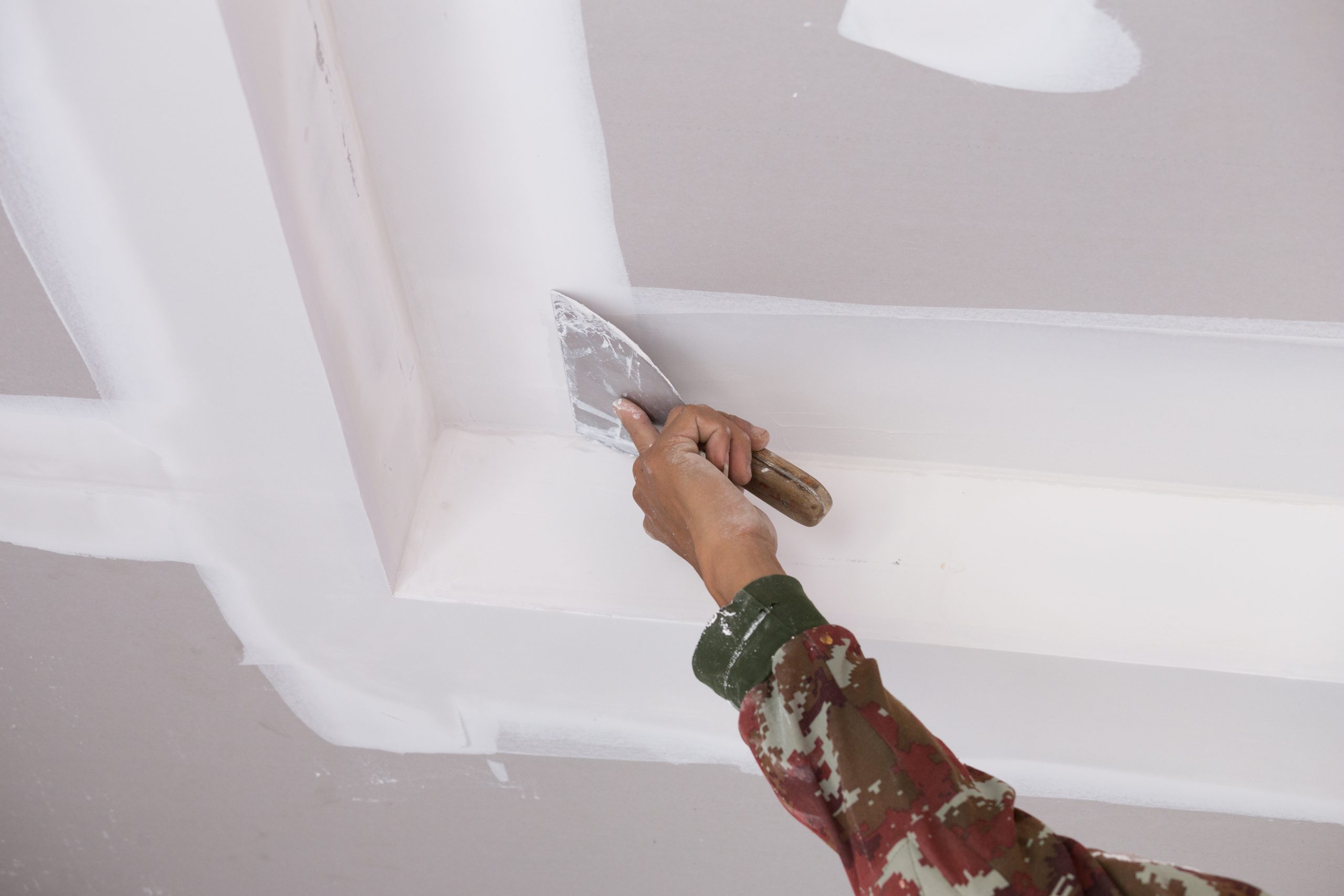 hand of worker using gypsum plaster ceiling joints at construction site